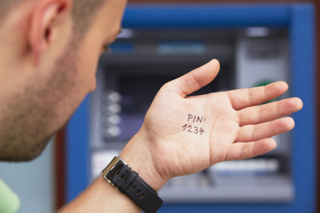 Mann guckt am Bankautomaten die Kontopin von seiner Hand ab.