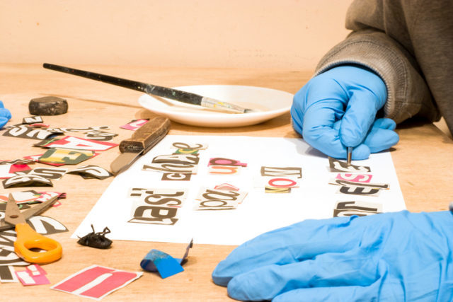 Ein Mann mit Handschuhen erstellt einen Erpresserbrief mit ausgeschnittenen Buchstaben aus der Zeitung